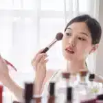 Young beautiful Asian woman applying cosmetics make up on he min